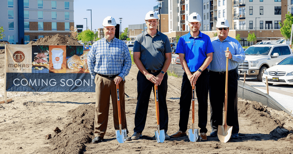 Four men in hard hats with shovels on the plot of land where construction on a new Mokas will soon take place.