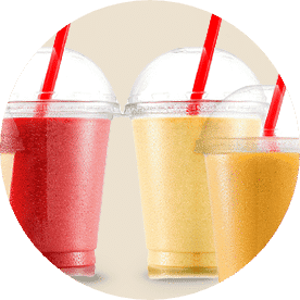 Three different smoothies in plastic cups with domed lids and red straws. From left to right, a red smoothie, a yellow smoothie and lastly an orange smoothie.