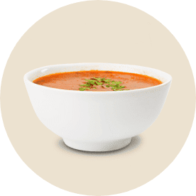 A white bowl filled with creamy red tomato soup with a small amount basil on top.