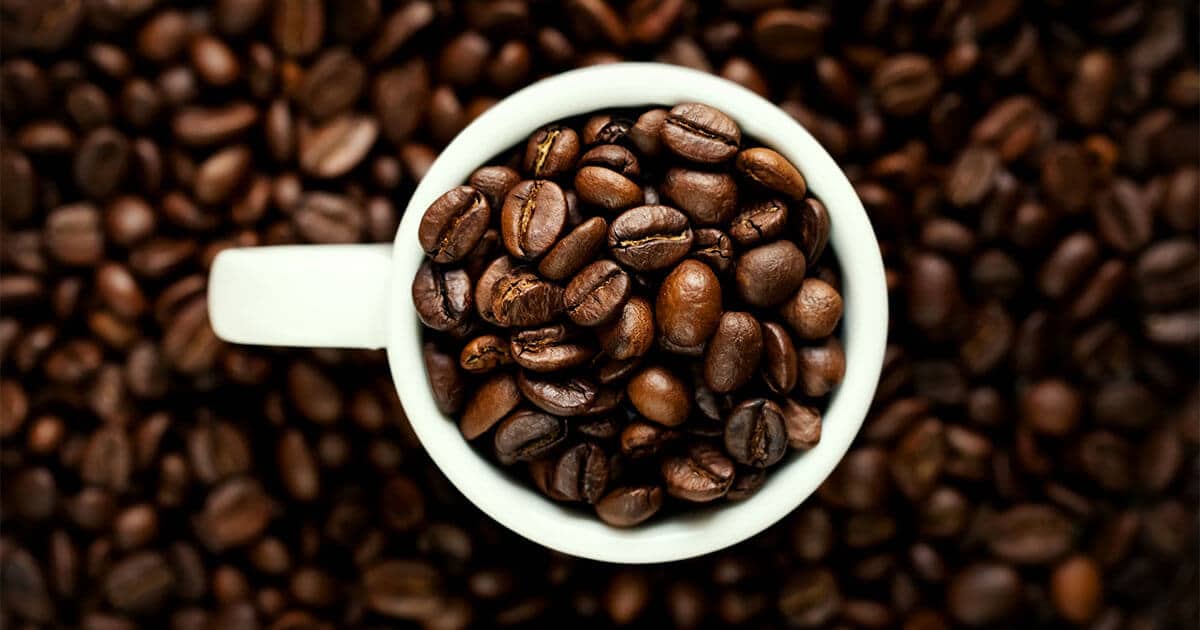 A cup full of coffee beans fill the brim of a coffee mug