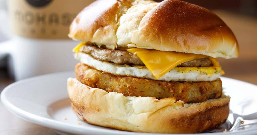 Breakfast slider with cheese, egg, sausage, and potato pancake on a white plate