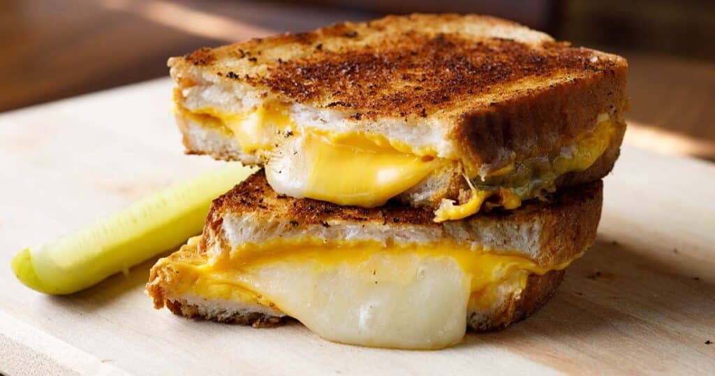 Grilled cheese sandwich on a wood board with a pickle spear