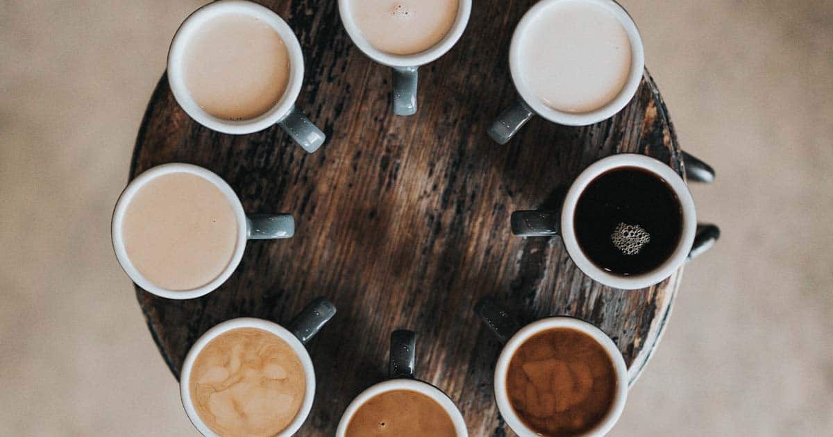 Multiple cups of coffee in a circle on a round wooden table