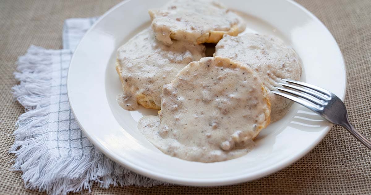 Biscuits and gravy on a white plate with a fork and blue and white tablecloth